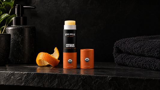 King Rilla Citrus lip balm on a charcoal shelf with a citrus peel accent.