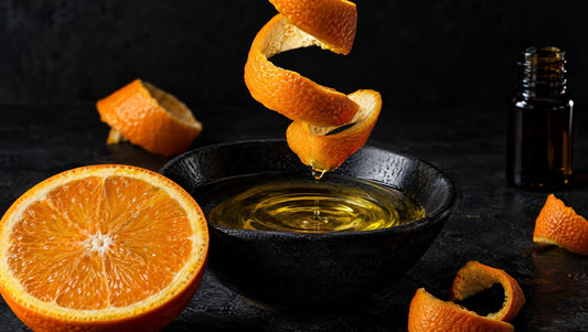 Fresh orange peel and golden oil in a black bowl against a dark background.