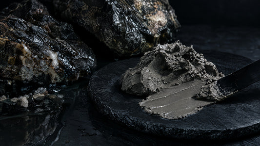 A mineral-mud smear and dark cosmetic spatula on black stone.