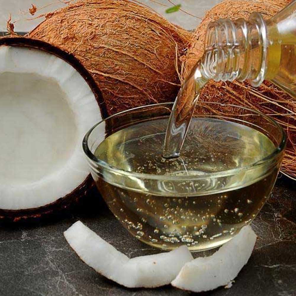 Coconut oil being poured into a glass bowl with coconuts around it.